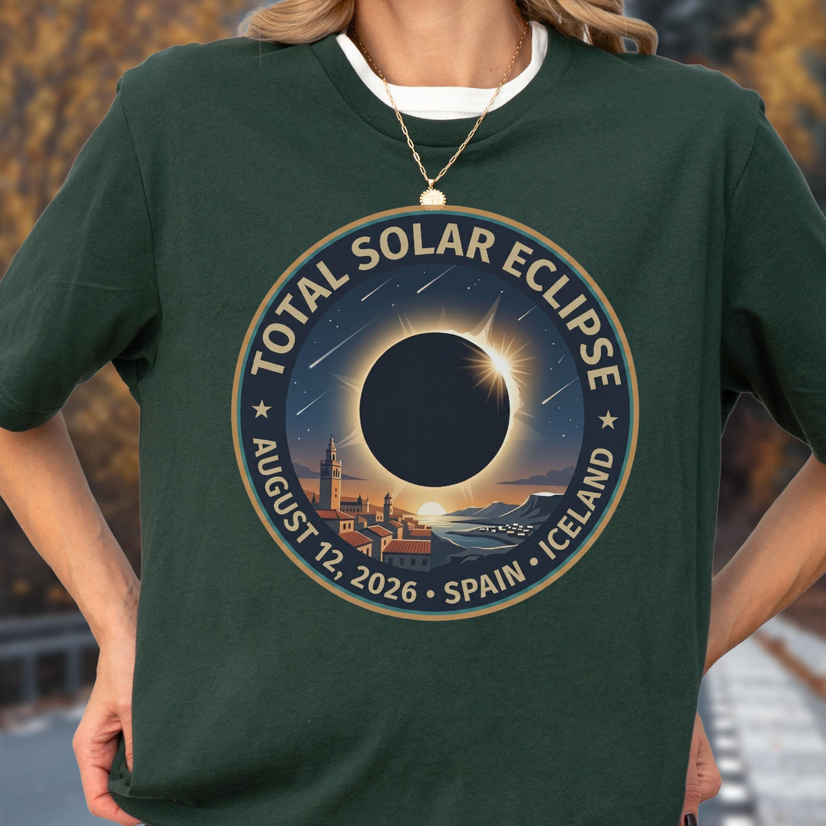 May include: A dark green t-shirt featuring a circular graphic of a total solar eclipse over a coastal town. The text reads TOTAL SOLAR ECLIPSE AUGUST 12, 2026 SPAIN ICELAND. The design includes a dark sun, a bright corona, and a starry night sky.