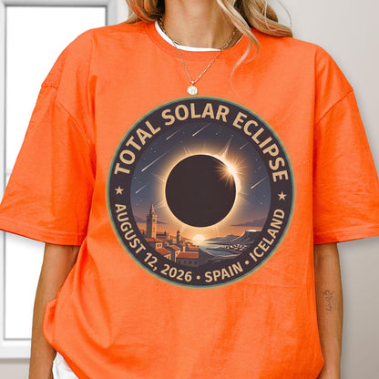 May include: A bright orange short-sleeve t-shirt featuring a circular graphic of a total solar eclipse over a coastal town. The text reads TOTAL SOLAR ECLIPSE AUGUST 12, 2026 SPAIN ICELAND. The design includes a dark sun, light rays, and stars.
