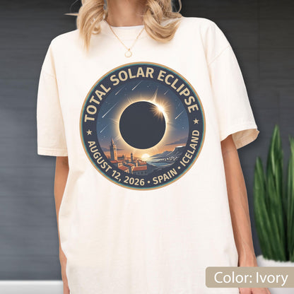 May include: An ivory short-sleeve t-shirt featuring a circular graphic of a total solar eclipse over a coastal town. The text reads Total Solar Eclipse, August 12, 2026, Spain, Iceland. The design includes a dark sun, stars, and a horizon line.