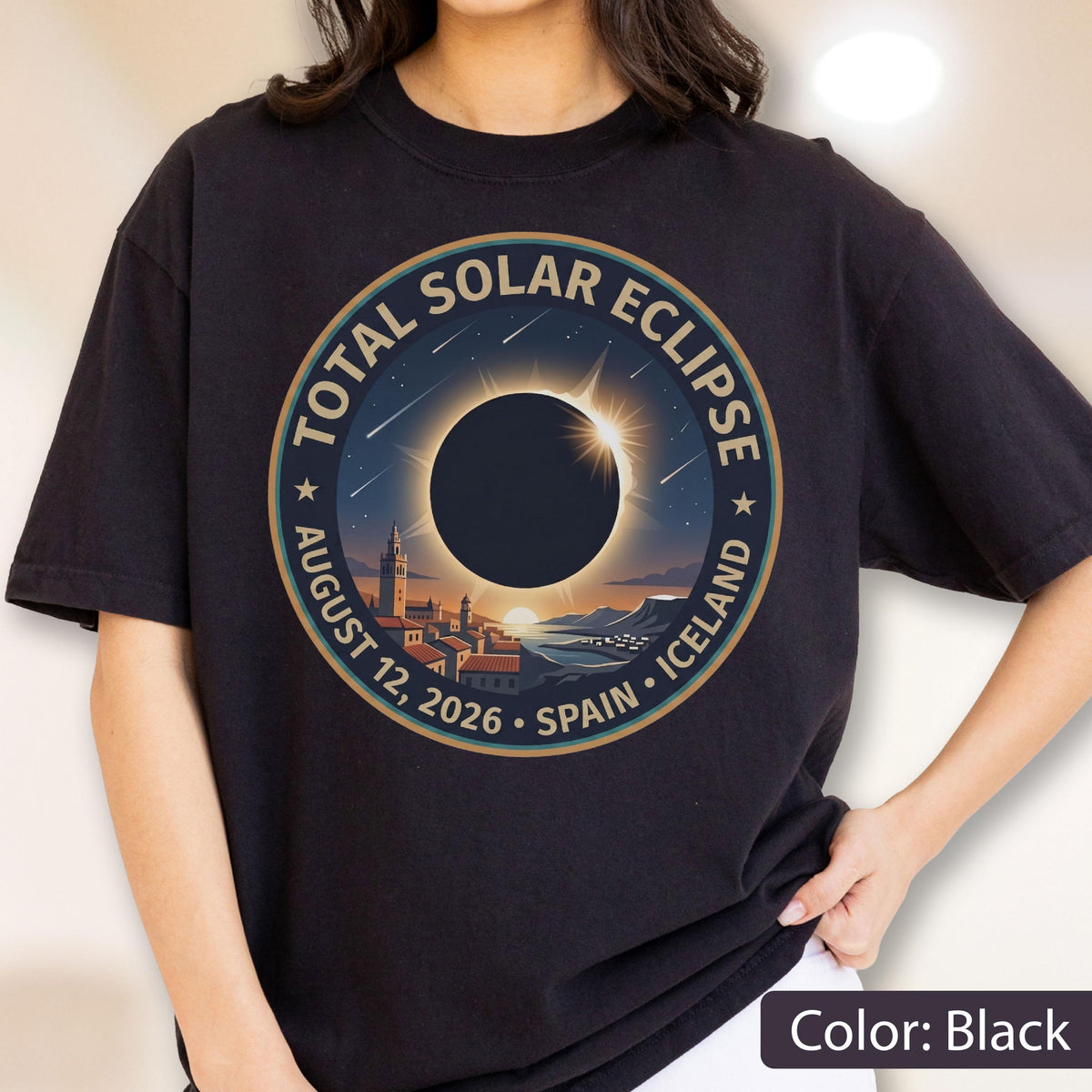 May include: A black t-shirt featuring a circular graphic of a total solar eclipse over a coastal town. The text reads TOTAL SOLAR ECLIPSE AUGUST 12, 2026 SPAIN ICELAND. The design includes a dark sun, a bright corona, and a landscape with buildings.