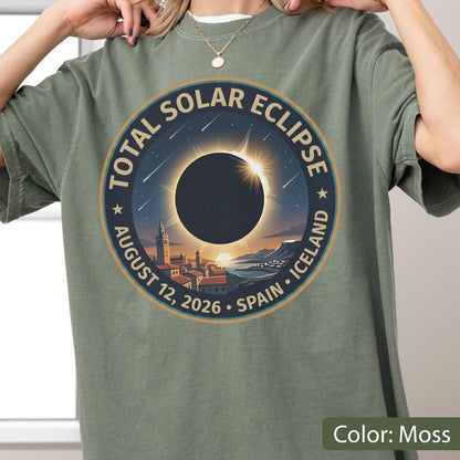 May include: A moss green t-shirt featuring a circular graphic of a total solar eclipse over a coastal town. The text reads TOTAL SOLAR ECLIPSE, AUGUST 12, 2026, SPAIN, ICELAND. The design includes a dark sun, bright corona, and falling stars.