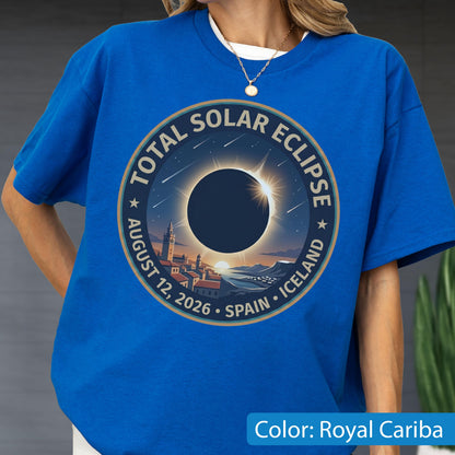 May include: A royal blue t-shirt featuring a circular graphic of a total solar eclipse over a coastal town. The text reads TOTAL SOLAR ECLIPSE AUGUST 12, 2026 SPAIN ICELAND. The design includes a dark moon, a bright sun corona, and stars.