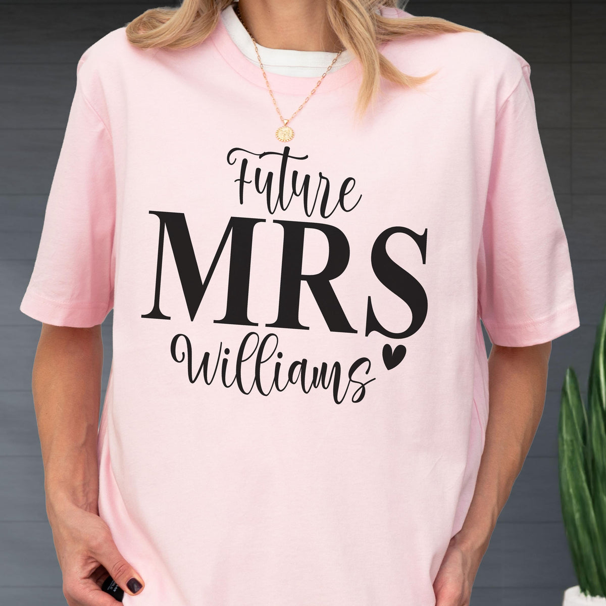 May include: A light pink short-sleeved t-shirt featuring black text that reads Future MRS Williams with a small heart icon. The shirt has a crew neckline and is made of a solid-colored fabric, providing a simple and clean look for casual wear.