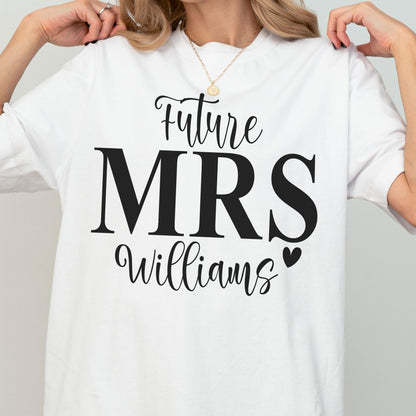 May include: A white short-sleeved t-shirt featuring black text that reads Future MRS Williams with a small black heart icon. The design is centered on the chest area of the garment, utilizing a combination of script and bold serif typography.