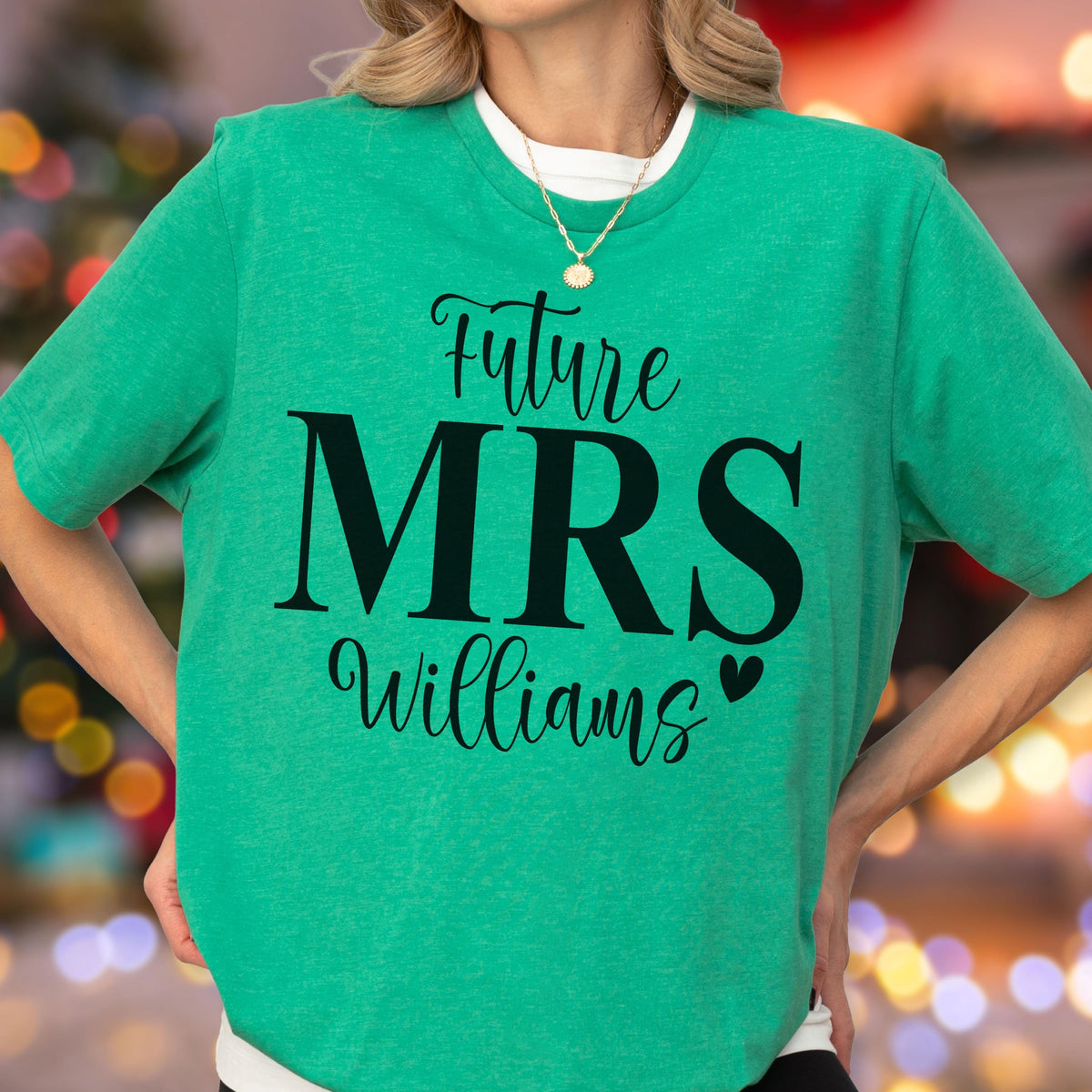 May include: A bright green short-sleeved t-shirt featuring the black text Future MRS Williams with a small heart icon. The shirt has a crew neckline and is worn over a white base layer, complemented by a delicate gold chain necklace with a round pendant.