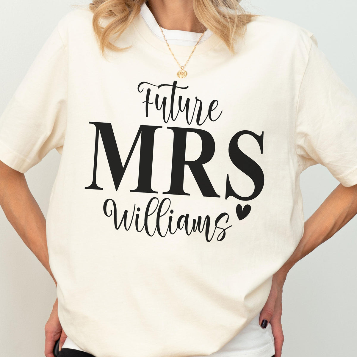 May include: A cream-colored short-sleeve t-shirt featuring black text that reads Future MRS Williams with a small heart icon. The design is centered on the chest of the garment, which is worn with a simple gold chain necklace.
