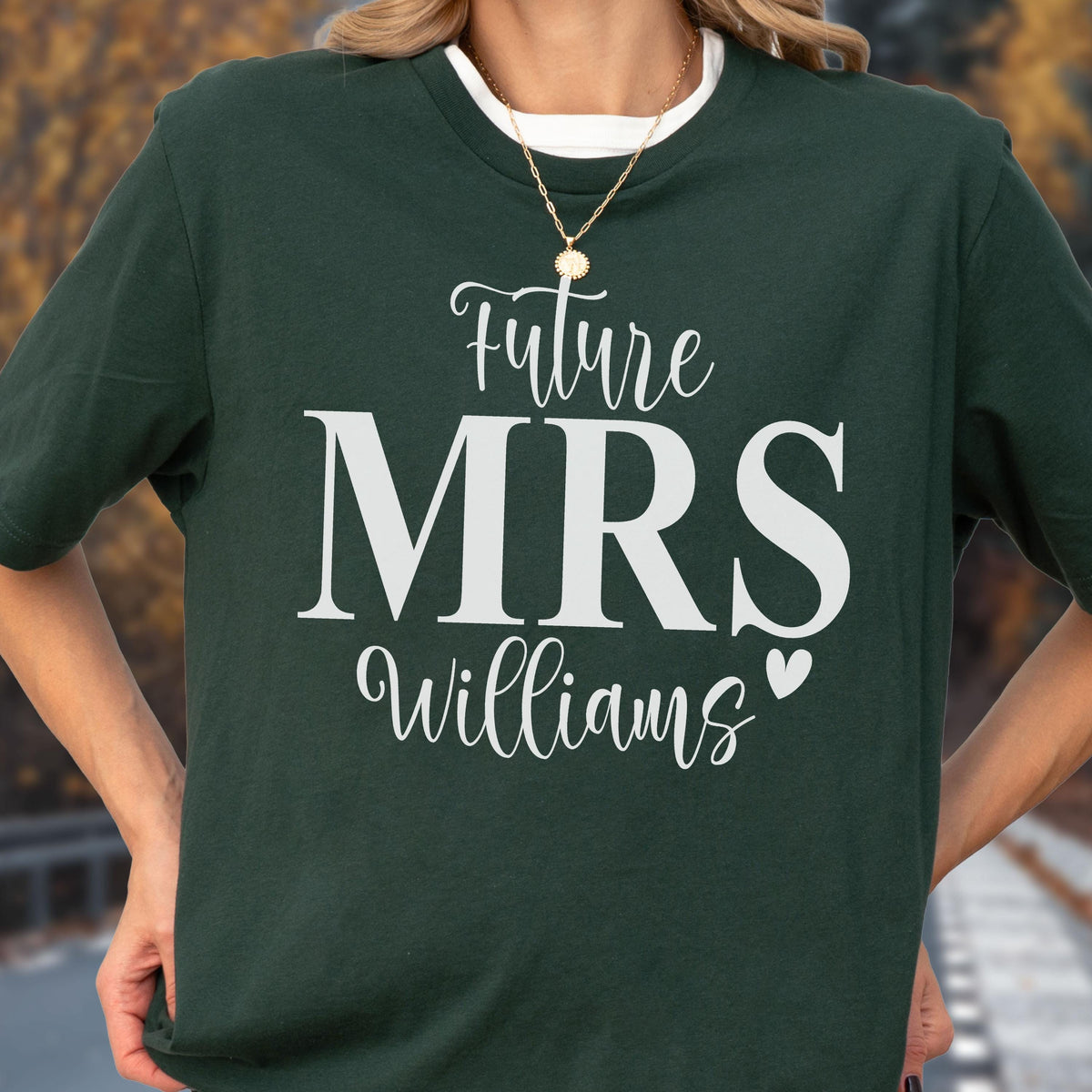 May include: A dark forest green short-sleeve t-shirt featuring white screen-printed text that reads Future MRS Williams with a small heart icon. The shirt has a crew neckline and is worn with a thin gold-toned chain necklace.