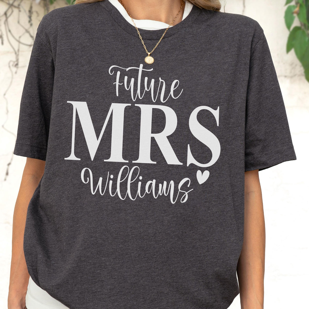 May include: A dark charcoal gray short-sleeved t-shirt featuring white screen-printed text that reads Future MRS Williams with a small heart icon. The shirt has a crew neckline and is made of a heathered fabric with a visible texture throughout.