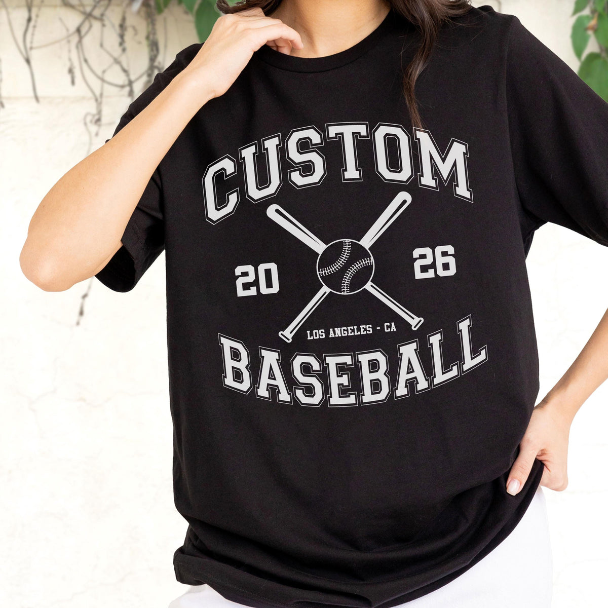 May include: A black short-sleeved t-shirt featuring a white graphic design with the text CUSTOM BASEBALL, the numbers 20 and 26, and an illustration of two crossed baseball bats behind a baseball, with the text LOS ANGELES - CA below.