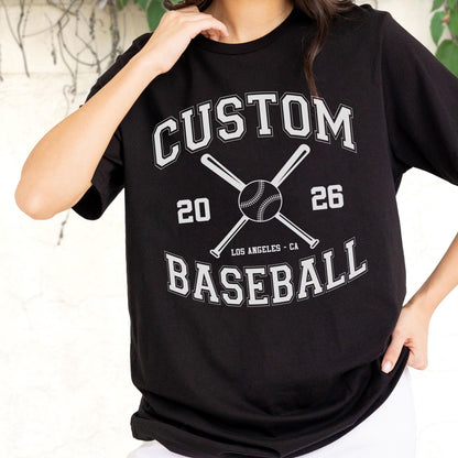May include: A black short-sleeved t-shirt featuring a white graphic design with the text CUSTOM BASEBALL, the numbers 20 and 26, and an illustration of two crossed baseball bats behind a baseball, with the text LOS ANGELES - CA below.