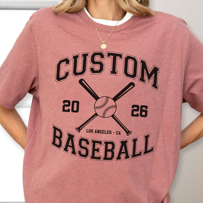May include: A mauve short-sleeve t-shirt featuring a black graphic with the text CUSTOM BASEBALL, the numbers 20 and 26, and an illustration of two crossed baseball bats with a baseball in the center, including the text LOS ANGELES - CA.