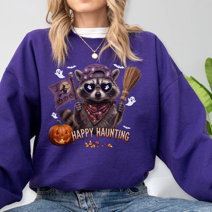 May include: A purple long-sleeve sweatshirt featuring a graphic of a raccoon wearing a baseball cap and heart-shaped sunglasses. The raccoon holds a broom and a flag with a witch silhouette. Text reads Happy Haunting above a pumpkin and candy.