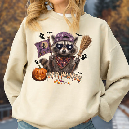 May include: A cream-colored crewneck sweatshirt featuring a graphic of a raccoon wearing a purple baseball cap, heart-shaped sunglasses, and a patterned bandana. The raccoon holds a broom and a flag with a witch silhouette, with a pumpkin and the text HAPPY HAUNTING.