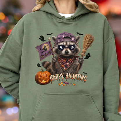 May include: An olive green hooded sweatshirt featuring a graphic of a raccoon wearing a purple baseball cap and heart-shaped sunglasses. The raccoon holds a broom and a flag with a witch silhouette. Text reads HAPPY HAUNTING with pumpkins and candy.