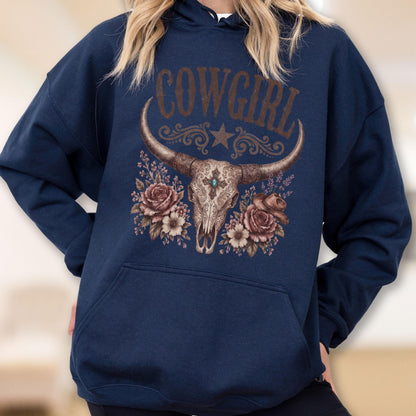 May include: A navy blue hooded sweatshirt featuring a graphic print of a longhorn skull, roses, and a small hat. The word COWGIRL is printed in brown above the skull, which is decorated with a turquoise stone and ornate scrollwork patterns.