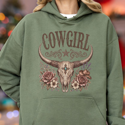 May include: An olive green hooded sweatshirt featuring a graphic print of a steer skull with ornate filigree, a central turquoise stone, and floral accents. The text COWGIRL is printed in a brown, distressed font above the steer skull design.