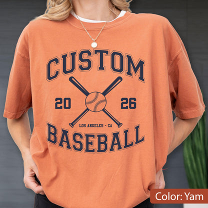 May include: A yam-colored short-sleeve t-shirt featuring a dark navy blue graphic print. The design includes the text CUSTOM BASEBALL, the numbers 20 and 26, and an illustration of two crossed baseball bats behind a central baseball.
