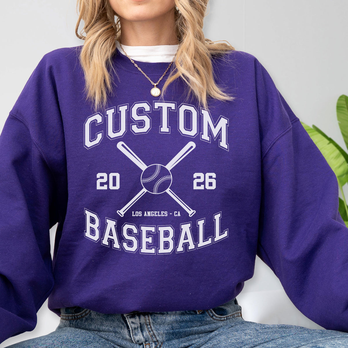 May include: A purple long-sleeve sweatshirt featuring a white graphic print with the text CUSTOM BASEBALL, the numbers 20 and 26, the location LOS ANGELES - CA, and an illustration of a baseball centered between two crossed baseball bats.