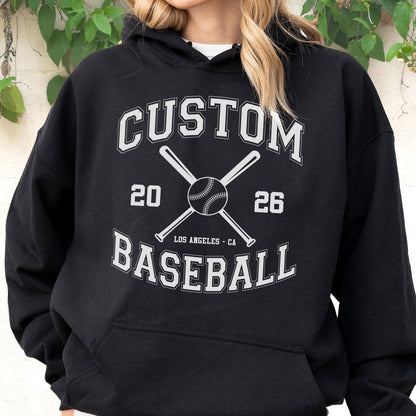 May include: A black hooded sweatshirt featuring a white graphic print with the text CUSTOM BASEBALL, the numbers 20 and 26, and the words LOS ANGELES CA. The design includes a central illustration of a baseball crossed with two baseball bats.