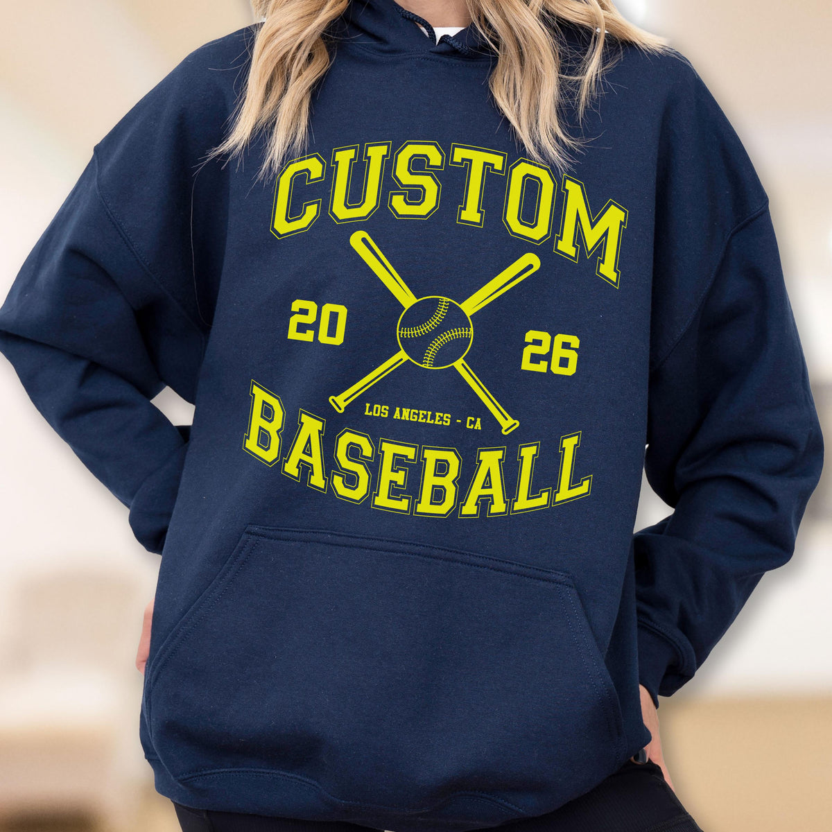 May include: A navy blue hooded sweatshirt featuring a yellow graphic print. The design includes two crossed baseball bats, a baseball, the text CUSTOM BASEBALL, the numbers 20 and 26, and the location text LOS ANGELES - CA in a collegiate font.
