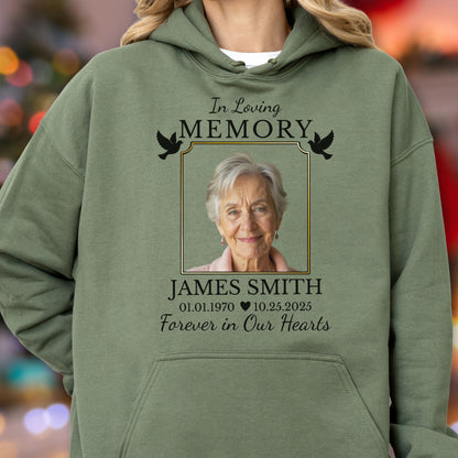 May include: An olive green hooded sweatshirt featuring a memorial graphic with the text In Loving Memory, the name James Smith, the dates 01.01.1970 and 10.25.2025, and the phrase Forever in Our Hearts, centered around a framed portrait of an older person.