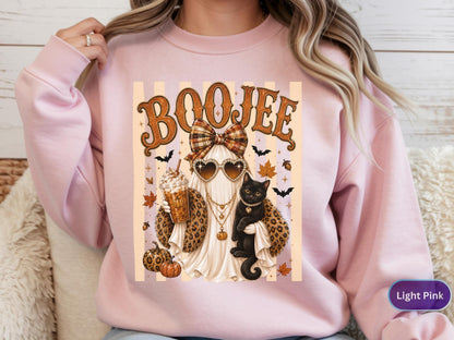 May include: A light pink crewneck sweatshirt featuring a graphic print of a ghost wearing heart-shaped sunglasses, a plaid bow, and a leopard print shawl. The ghost holds an iced coffee and a black cat. The text BOOJEE is printed above.
