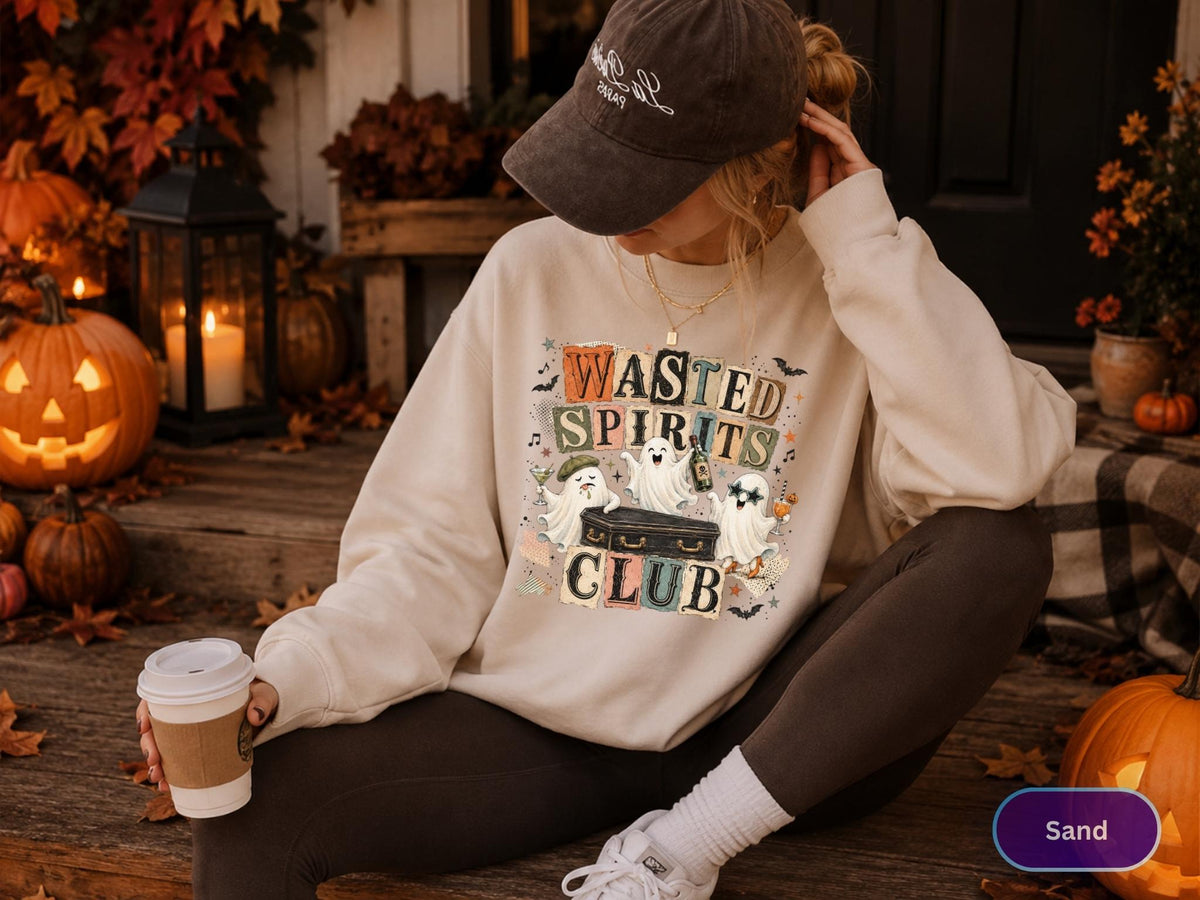 May include: A beige crewneck sweatshirt featuring a graphic print of three cartoon ghosts around a black coffin with the text Wasted Spirits Club. The design includes colorful block letters, small bats, and stars. The sweatshirt has long sleeves.
