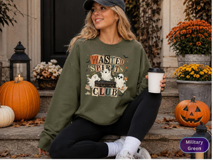 May include: A military green crewneck sweatshirt featuring a graphic print with the text "WASTED SPIRITS CLUB" and three cartoon ghosts interacting with a black trunk, surrounded by small bats and stars in a vintage-inspired color palette.