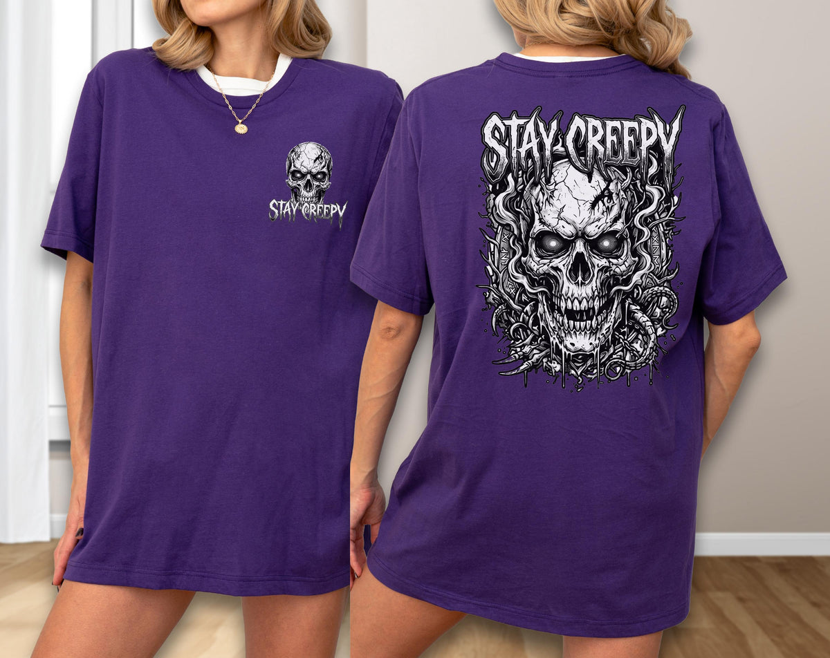 May include: A purple short-sleeve t-shirt featuring a small skull graphic with the text STAY CREEPY on the front left chest and a large, detailed black and white skull illustration with the text STAY CREEPY printed on the back.