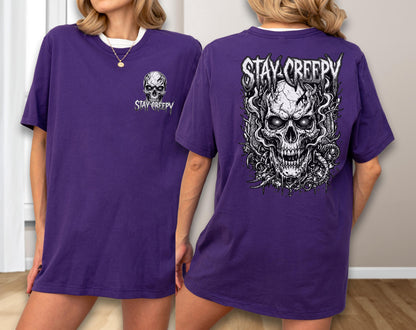 May include: A purple short-sleeve t-shirt featuring a small skull graphic with the text STAY CREEPY on the front left chest and a large, detailed black and white skull illustration with the text STAY CREEPY printed on the back.