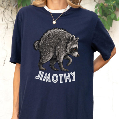 May include: A navy blue t-shirt featuring a graphic illustration of a raccoon with intricate leaf-like patterns in its fur. Below the raccoon, the text JIMOTHY is printed in bold, white, sans-serif capital letters. The shirt has short sleeves.