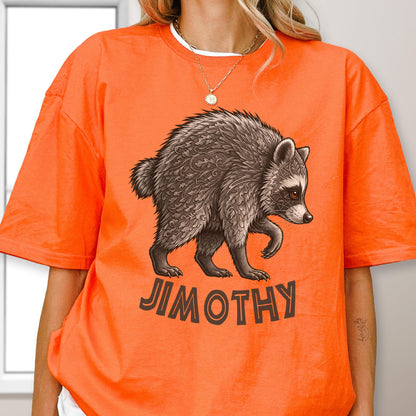 May include: A bright orange t-shirt featuring a detailed brown raccoon illustration with intricate leaf and geometric patterns on its fur. Below the raccoon, the name JIMOTHY is printed in bold, dark brown capital letters. The shirt has a crew neckline.