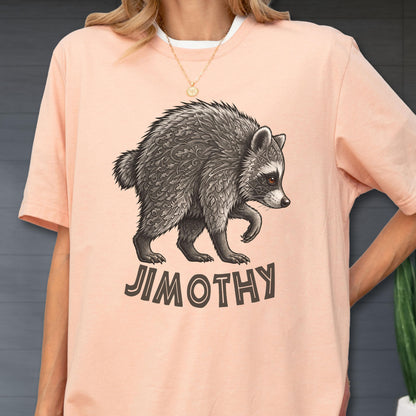 May include: A peach-colored t-shirt featuring a graphic illustration of a raccoon with intricate leaf and geometric patterns on its fur. Below the raccoon, the name JIMOTHY is printed in bold, dark brown, sans-serif capital letters.