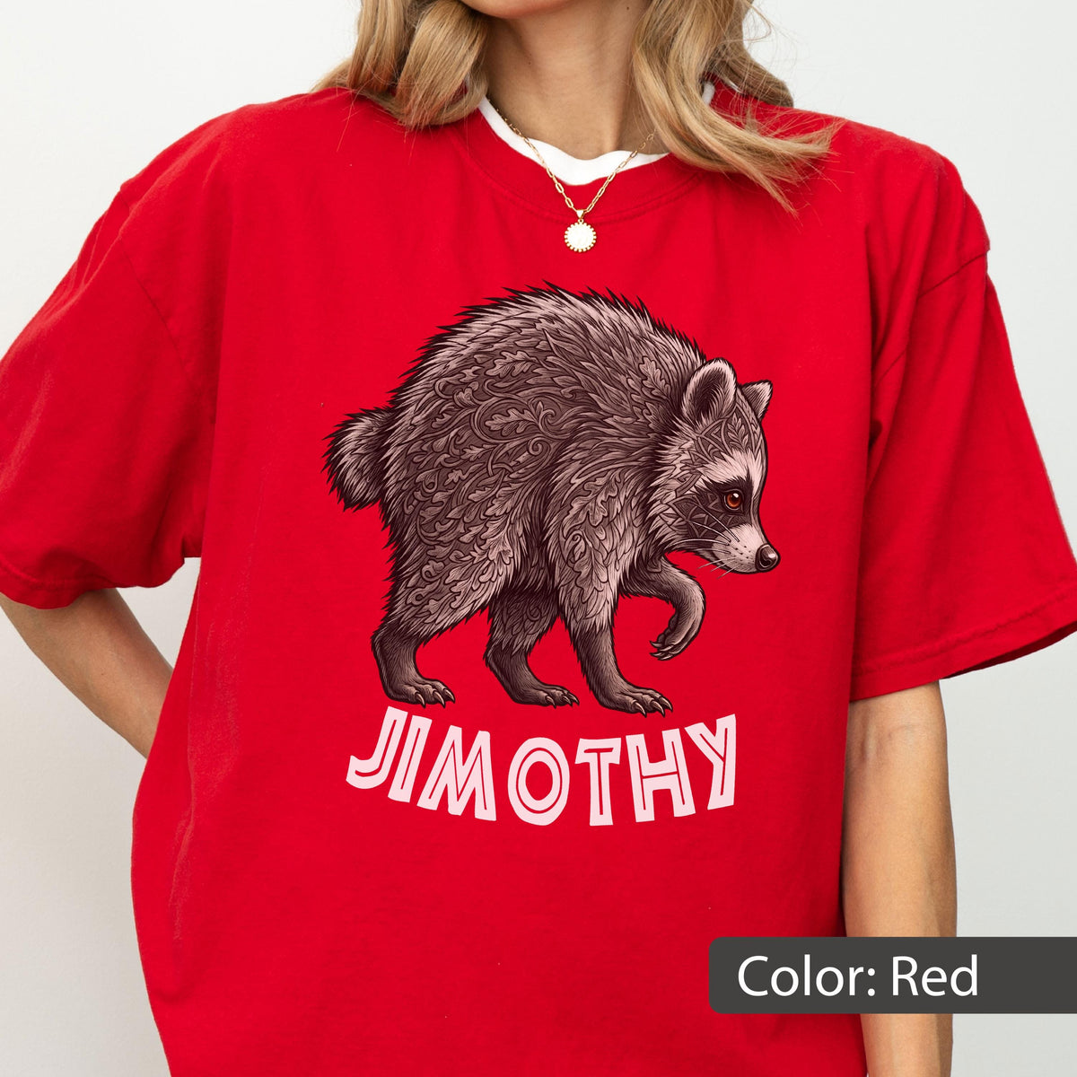 May include: A bright red short-sleeved t-shirt featuring a graphic of a raccoon with intricate leaf-like patterns in its fur. Below the raccoon, the name JIMOTHY is printed in bold, light pink capital letters. The shirt has a crew neckline.