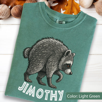 May include: A light green crew neck t-shirt featuring a graphic of a raccoon with intricate leaf-patterned fur. The raccoon is depicted in shades of gray and black. Below the animal, the text JIMOTHY is printed in large, bold, white capital letters.