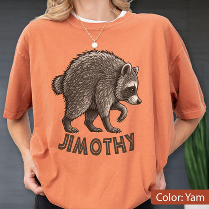 May include: A burnt orange crewneck t-shirt featuring a graphic of a raccoon with intricate leaf-like patterns in its fur. Below the raccoon, the name JIMOTHY is printed in a bold, dark brown, sans-serif font. The shirt has short sleeves.