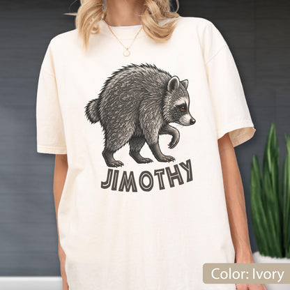 May include: An ivory short-sleeve t-shirt featuring a detailed graphic of a raccoon with intricate leaf-like patterns on its fur. Below the raccoon, the text JIMOTHY is printed in a bold, dark, sans-serif font. The shirt has a crew neckline.