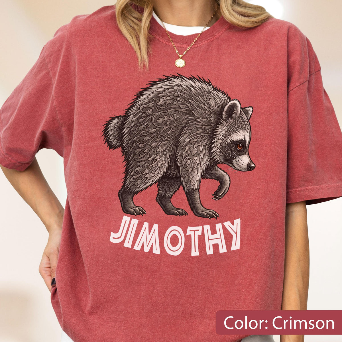 May include: A crimson short-sleeved t-shirt featuring a graphic illustration of a raccoon with intricate leaf-like patterns on its fur. Below the raccoon, the name JIMOTHY is printed in bold, light-colored capital letters on the front of the shirt.