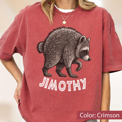 May include: A crimson short-sleeved t-shirt featuring a graphic illustration of a raccoon with intricate leaf-like patterns on its fur. Below the raccoon, the name JIMOTHY is printed in bold, light-colored capital letters on the front of the shirt.