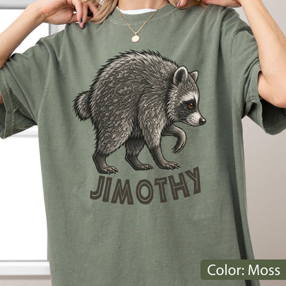 May include: A moss green t-shirt featuring a graphic illustration of a raccoon with intricate leaf-like patterns in its fur. Below the raccoon, the name JIMOTHY is printed in bold, dark brown capital letters. The shirt has a crew neckline.