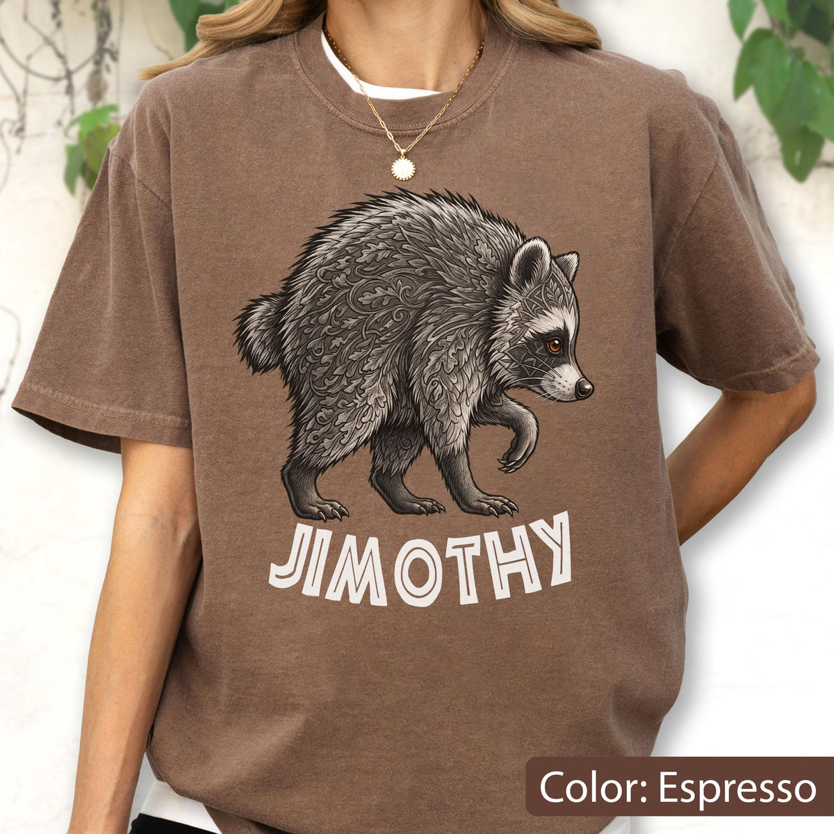 May include: An espresso-colored t-shirt featuring a graphic of a raccoon with intricate leaf-like patterns in its fur. Below the raccoon, the text JIMOTHY is printed in a bold, white, sans-serif font. The shirt has a crew neckline and short sleeves.