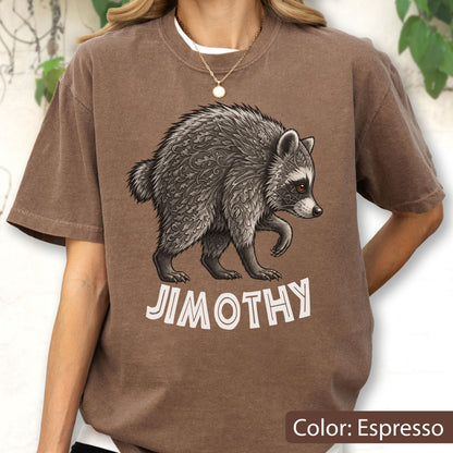 May include: An espresso-colored t-shirt featuring a graphic of a raccoon with intricate leaf-like patterns in its fur. Below the raccoon, the text JIMOTHY is printed in a bold, white, sans-serif font. The shirt has a crew neckline and short sleeves.