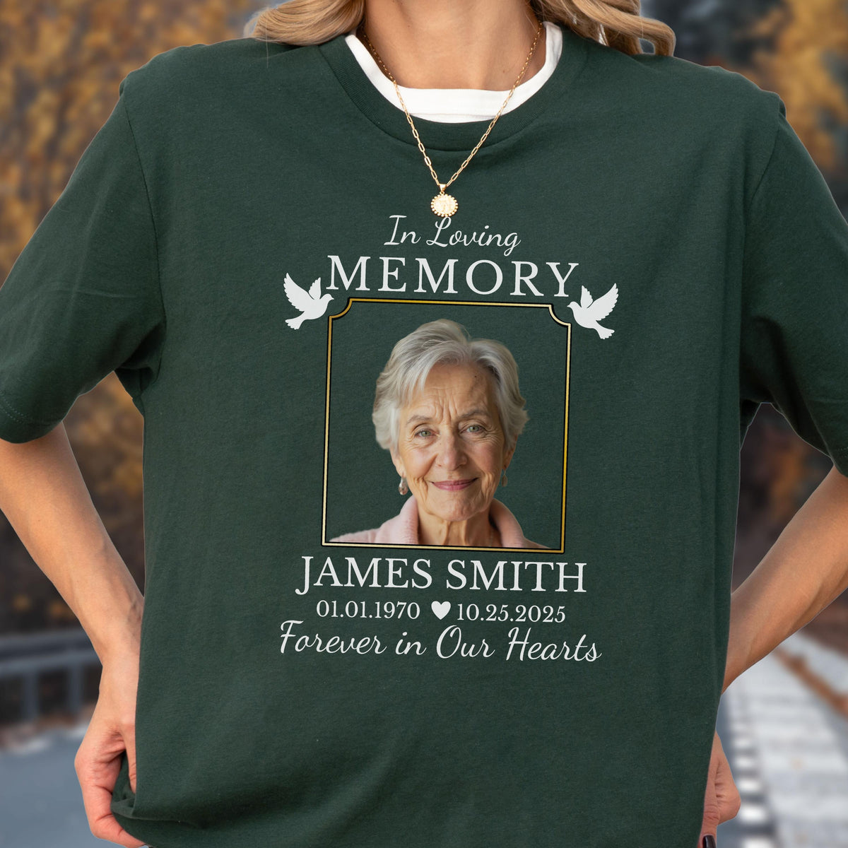 May include: A dark green t-shirt featuring a memorial design with a central photograph of an older person. The text reads In Loving Memory, James Smith, 01.01.1970, 10.25.2025, and Forever in Our Hearts, accompanied by two white dove illustrations.