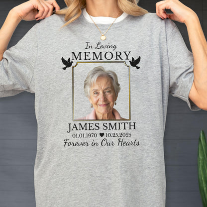 May include: A heather gray t-shirt featuring a memorial design with the text In Loving Memory, a framed photograph of an older person, the name JAMES SMITH, the dates 01.01.1970 and 10.25.2025 separated by a heart, and the text Forever in Our Hearts.