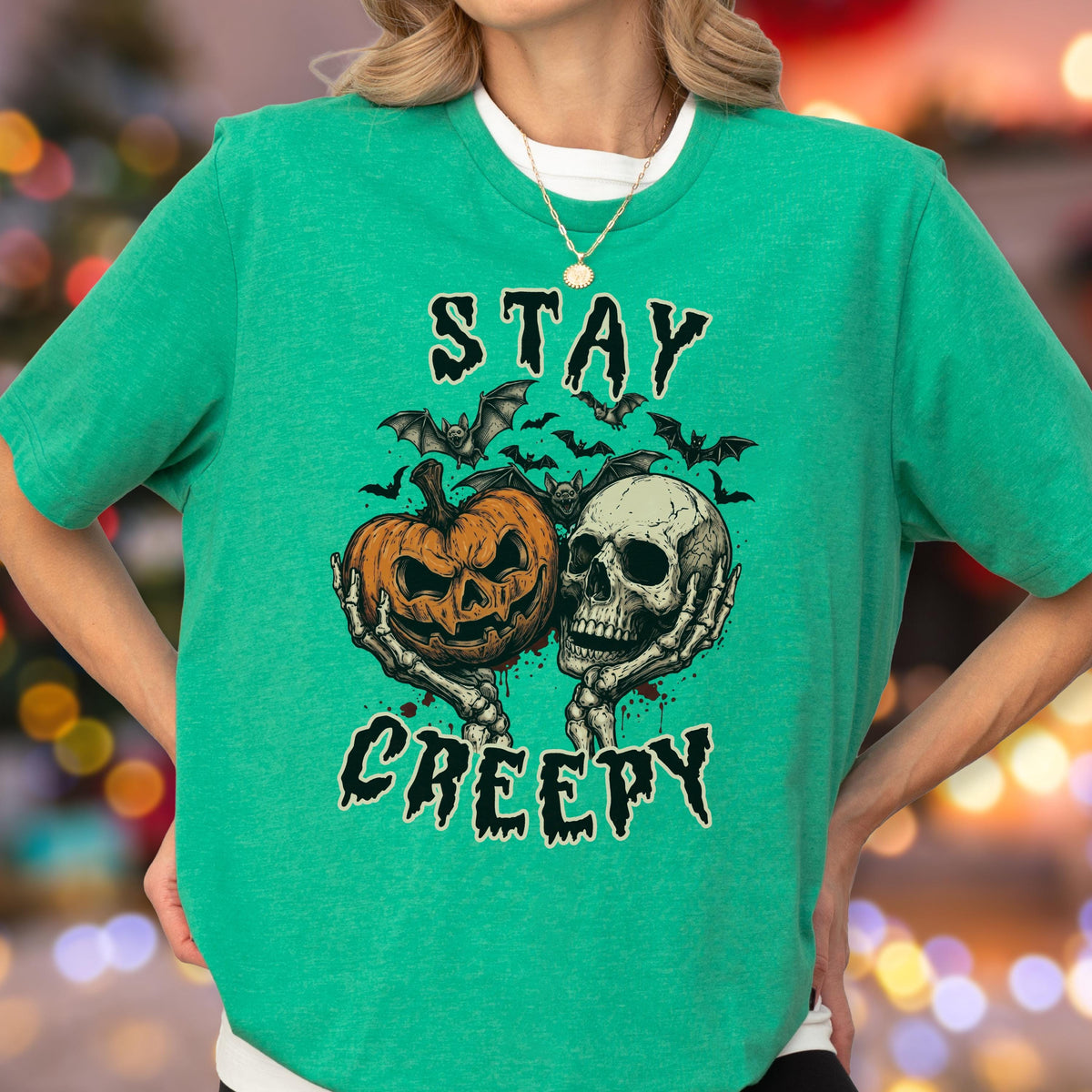 May include: A bright green short-sleeve t-shirt featuring a graphic print of a jack-o'-lantern and a human skull held by skeletal hands, surrounded by bats. The text "STAY CREEPY" is printed in a distressed black font above and below the graphic.