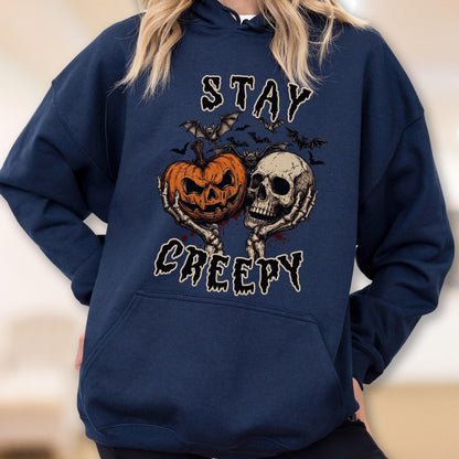 May include: A navy blue hooded sweatshirt featuring a graphic print of two skeletal hands holding a carved orange jack-o'-lantern and a human skull. Above and below the central illustration, the text reads STAY CREEPY in a stylized font.