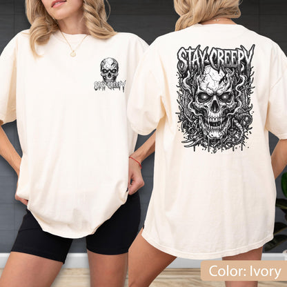 May include: An ivory t-shirt featuring a black graphic print of a skull and the text "STAY CREEPY." The front displays a small skull logo on the left chest, while the back showcases a large, detailed skull illustration surrounded by intricate line art.
