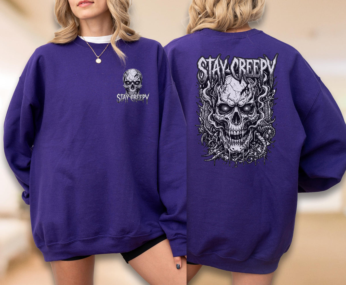 May include: A deep purple long-sleeve sweatshirt featuring a small graphic of a skull and the text "STAY CREEPY" on the front left chest, and a large, detailed illustration of a skull with smoke and the text "STAY CREEPY" on the back.