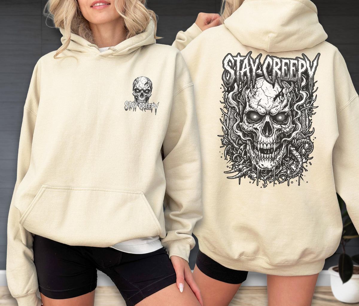 May include: A cream-colored hooded sweatshirt featuring a black and white graphic print. The front displays a small skull with the text "STAY CREEPY," while the back showcases a large, detailed skull illustration surrounded by smoke and the text "STAY CREEPY."