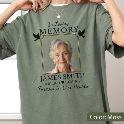 May include: A moss green t-shirt featuring a memorial graphic with a photograph of an older person inside a gold-bordered frame. The text reads In Loving Memory, JAMES SMITH, 01.01.1970, 10.25.2025, and Forever in Our Hearts, with two black doves.